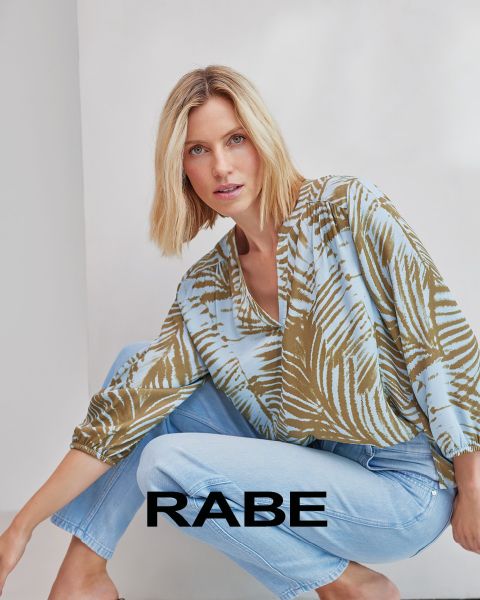 Una mujer posa frente a una pared blanca, vistiendo un chaleco rojo sin mangas sobre una blusa a rayas rojas y blancas y pantalones oscuros. En la parte inferior de la imagen se puede leer la palabra "CUERVO".