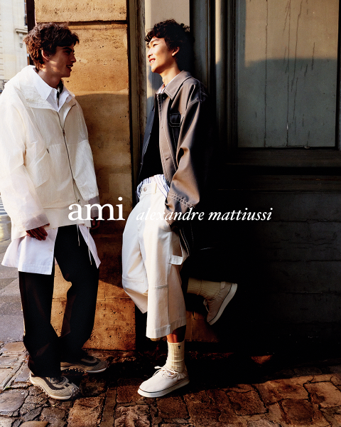 Tres personas de pie muy juntas con atuendos elegantes, una sostiene una bebida en la mano. El texto "ami alexandre mattiussi" está superpuesto en letras blancas sobre la imagen. No se ven sus rostros.