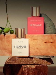 Un frasco del perfume "Hundred Silent Ways" de Nishane con una tapa dorada que se refleja abajo y un fondo rojo y negro difuminado.