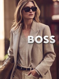 Una mujer con cabello largo y oscuro y maquillaje neutro lleva una chaqueta de shearling marrón y un jersey de cuello alto beige, y mira directamente a la cámara con una expresión tranquila frente a un fondo sencillo.
