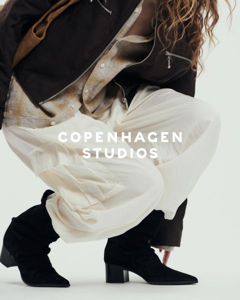 Una persona con botas gruesas negras con cordones y pantalones oscuros está de pie sobre una superficie blanca. Parte de la imagen está oscurecida por hilo rosa y beige borroso. El texto "Copenhagen Studios" aparece sobre la foto.