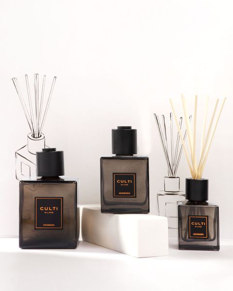 Una presentación elegante de productos de fragancias para el hogar de Culti Milano, que incluye velas, un difusor con varillas y botellas, todo en recipientes de color verde oscuro, sobre un fondo color oliva con el logo de Culti Milano debajo.