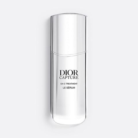 Un frasco delgado y translúcido de Dior Capture OX-C Treatment Le Sérum. El frasco es alto y curvo, con un diseño minimalista y texto negro en el frente. Sobre un fondo gris claro.