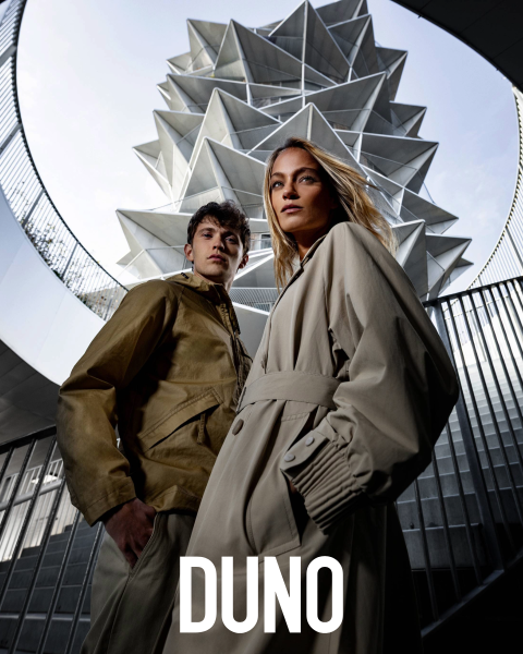 Una persona está de perfil, lleva una chaqueta amarilla clara y una falda blanca, tiene la cabeza inclinada hacia atrás y los ojos cerrados. Se encuentra en un entorno exterior con grandes cactus y palmeras. La palabra "DUNO" aparece verticalmente en el lado izquierdo de la imagen.