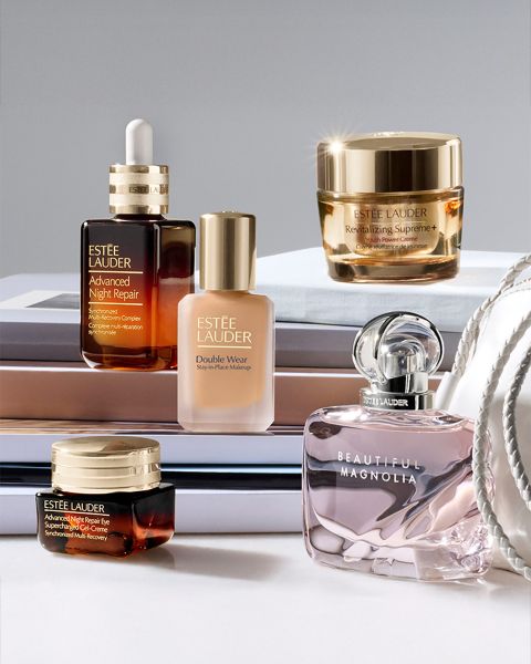 Una mujer con cabello largo posa con una botella de Estée Lauder Advanced Night Repair en primer plano. En el fondo, se ve un paisaje urbano nocturno. Un texto en alemán describe los beneficios del producto para el cuidado de la piel.