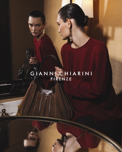 Persona con una gabardina larga de cuero negra y gafas de sol, sosteniendo un bolso pequeño con estampado de leopardo. El fondo es gris, con el texto "GIANNI CHIARINI FIRENZE" en blanco sobre la imagen.