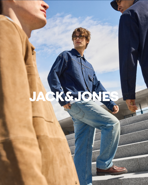 Dos hombres con atuendos de mezclilla están sentados frente a un fondo simple. El hombre de adelante se tapa la boca con la mano, mientras que el otro está sentado detrás de él. En el centro está el texto "JACK & JONES".