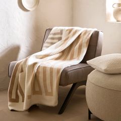 Una moderna silla redonda con un cojín suave se encuentra junto a cortinas estampadas y translúcidas al lado de una ventana. Un cojín a juego está en el suelo de madera y una luz suave entra por la ventana, creando un ambiente acogedor.