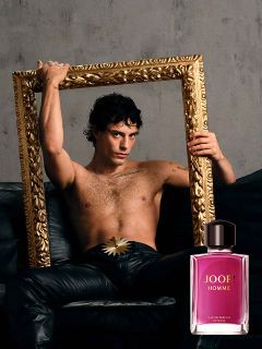 Una botella de JOOP! Homme Le Parfum se sostiene frente a un fondo borroso con una flor de iris violeta. El logo dorado de "JOOP!" es claramente visible en la parte superior. La imagen transmite elegancia y lujo.