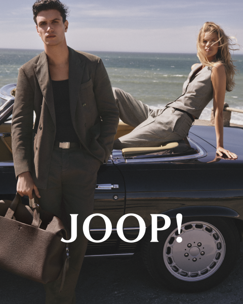 Hombre y mujer con ropa de verano elegante en un café. El hombre lleva una camisa beige y sostiene una taza, mientras que la mujer con un vestido claro sostiene un platillo. Ambos llevan gafas de sol. "JOOP!" se ve claramente.