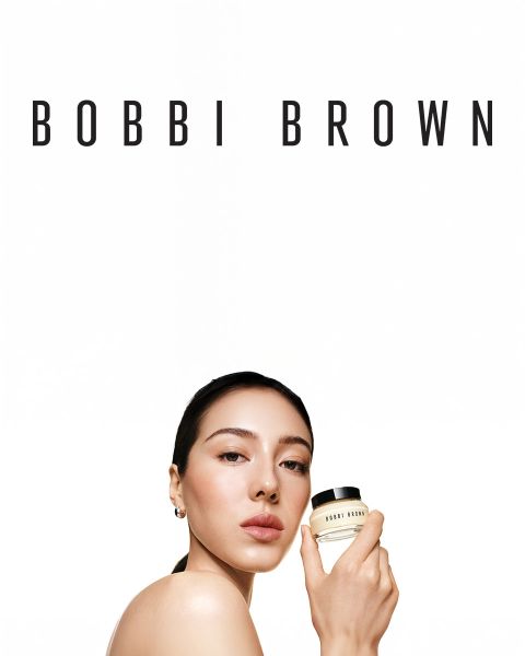 Una selección de lápices de sombra de ojos en crema de larga duración de Bobbi Brown en varios tonos, presentados horizontalmente sobre una superficie texturizada. Cada lápiz está abierto, revelando los colores cremosos. El nombre de la marca es visible en las tapas.