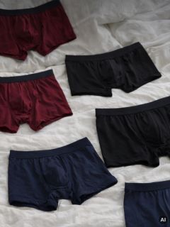 Seis pares de bóxers para hombre en negro, burdeos y azul marino se extienden sobre una base de tela blanca.