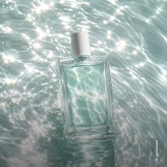 Un frasco de perfume rectangular de cristal con tapón blanco flota sobre agua reluciente y bañada por el sol.