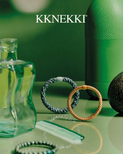 Una persona con un jersey azul marino y vaqueros sostiene un cepillo de pelo azul detrás de su espalda y lleva pulseras de cuentas turquesas. Arriba, el logotipo "KKNEKKI".