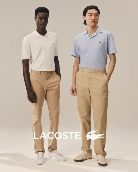 Cuatro modelos posan al aire libre con atuendos de Lacoste frente a un cielo azul. De izquierda a derecha: una persona con gabardina, una persona con suéter y pantalones, una persona con chaleco y falda y una persona con un chándal. El logo de Lacoste está en la parte inferior.