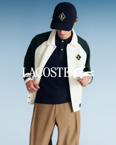Cuatro modelos posan al aire libre con atuendos de Lacoste frente a un cielo azul. De izquierda a derecha: una persona con gabardina, una persona con suéter y pantalones, una persona con chaleco y falda y una persona con un chándal. El logo de Lacoste está en la parte inferior.