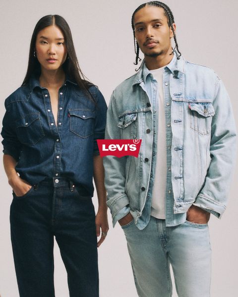 Hombre y mujer abrazándose frente a un fondo de mosaico azul, ambos con chaquetas y pantalones vaqueros. Encima de ellos, un logo rojo de Levi's destaca claramente.