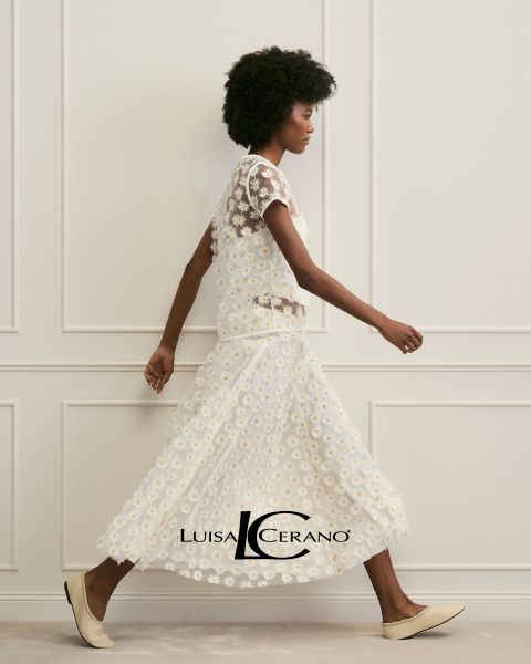 Una mujer con cabello castaño largo lleva un vestido floreado y una prenda de piel texturizada color óxido sobre el hombro. Mira directamente a la cámara. Abajo en el centro se ve el texto "Luisa Cerano".