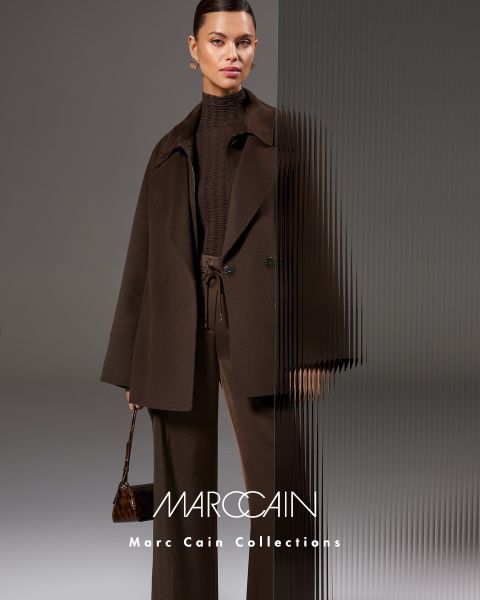 Una mujer posa con confianza con una chaqueta de cuero color burdeos y una falda con una bufanda gruesa y texturizada color burdeos. En el fondo se ve un cielo sombrío y el nombre de la marca "Marc Cain" se ve en la parte inferior.