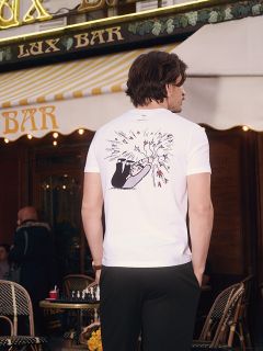 Una mujer está de pie en un baño y lleva una camiseta sin mangas púrpura atada a la cintura, ropa interior de talle alto a juego y medias transparentes. Está apoyada en un lavabo frente a paredes de color verde pálido y puertas de persiana.