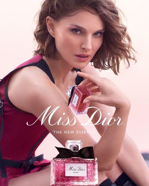 Un frasco dorado de perfume Dior, rodeado de mariposas doradas flotantes, lazo rosa y delicadas flores blancas con el texto "DIOR Because I Adore You".