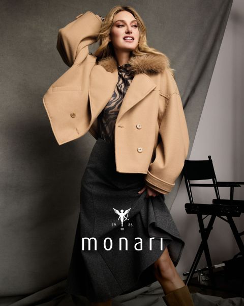 Una mujer con una capa de piel sintética sobre un top con estampado de leopardo y una falda marrón está sentada y posando; abajo se ven "monari" y el logo.