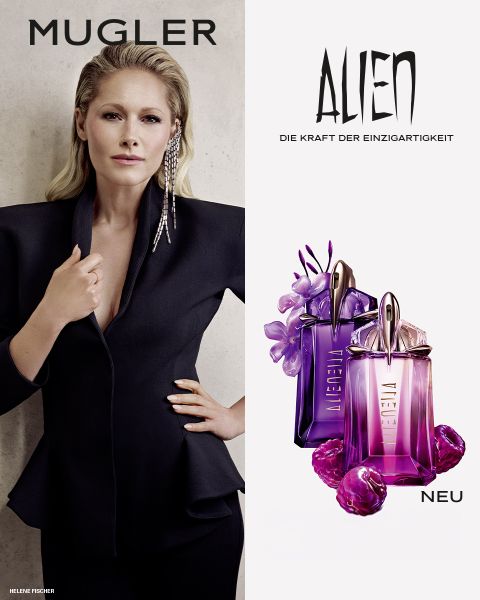 Una mujer con una piel oscura y radiante y un cabello negro liso posa delante de un fondo violeta. Delante de ella hay dos frascos de perfume Alien de Mugler. El texto dice "MUGLER" y "ALIEN EXTRA INTENSE LAS FRAGANCIAS RECARGABLES".