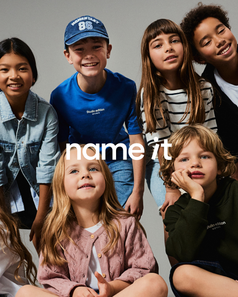 Un grupo de ocho niños diferentes están juntos frente a un fondo gris, todos vestidos con atuendos casuales a juego en colores neutros y pastel. El texto "name it" aparece en el centro de la imagen.
