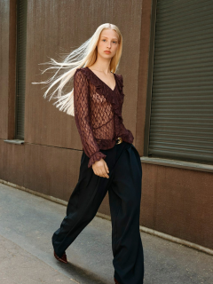 Mujer sentada en una escalera de piedra al aire libre, vestida con una blusa vaquera de manga larga con detalles de volantes y unos vaqueros a juego de talle alto. Tiene el pelo oscuro, lleva gafas de sol en la cabeza y mira pensativa a la distancia.