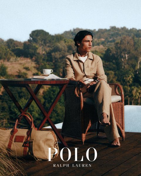 Un hombre y una mujer visten elegantes gabardinas de Ralph Lauren. El hombre combina su abrigo con un jersey colorido y pantalones grises, mientras que la mujer lleva una camisa a rayas, guantes marrones y un cinturón ancho. "POLO RALPH LAUREN" se muestra en letras blancas.