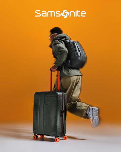 Maleta Samsonite de color verde claro con un patrón texturizado y cuatro ruedas. El asa es extensible. El gran logotipo de "Samsonite" se extiende a lo ancho de la maleta. El fondo tiene un diseño ondulado verde y blanco.