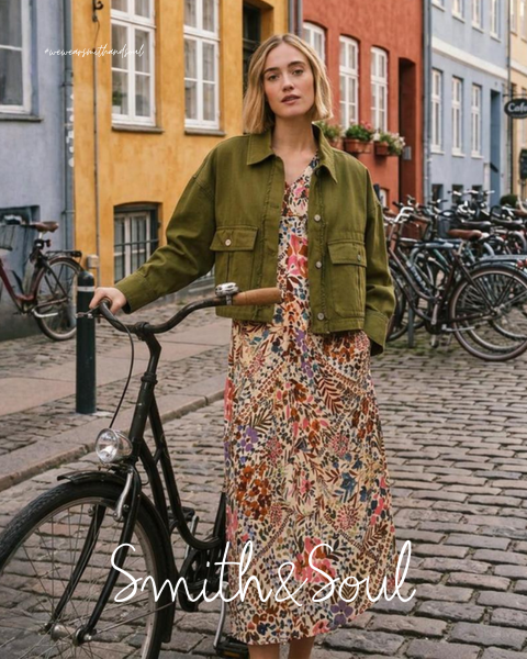 Una mujer con una camisa rosa y una chaqueta de punto con pantalones blancos posa delante de un fondo blanco. El texto dice "Smith & Soul" en la parte inferior.