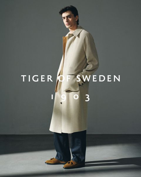 Dos hombres con abrigos elegantes están de pie al aire libre junto al agua bajo un cielo despejado. El texto "TIGER OF SWEDEN 1903" aparece en el centro de la imagen.