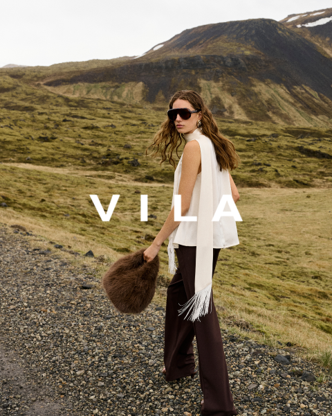 Cinco mujeres en ropa casual, incluyendo vaqueros y tops en colores neutros, están de pie juntas y sonriendo frente a un fondo sencillo. El texto superpuesto dice "Vila Clothes".