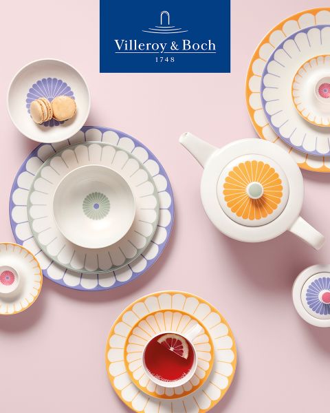Una exposición de cocina muestra un cuenco negro con pequeños batidores sobre una bandeja rectangular. Al lado hay un plato con tapa de cristal en el que hay queso y hierbas frescas. En la parte superior luce el logotipo de Villeroy & Boch.