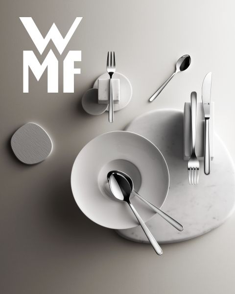 Una olla llena de higos, moras y guarniciones aromáticas está sobre una tabla de madera oscura. Encima de la olla se ve el logo de WMF. El fondo es una superficie oscura texturizada.