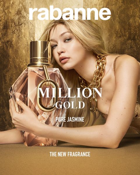 Una mujer con un vestido dorado y un collar grueso posa con un frasco de perfume grande y facetado que dice "Million Gold Pure Jasmine" de Rabanne. El fondo es dorado y en la parte inferior dice "LA NUEVA FRAGANCIA".