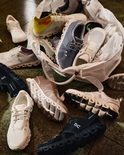 Una variedad de zapatillas de correr On en varios colores están esparcidas por el suelo, desbordándose de una bolsa de mano blanca, mostrando sus distintivas suelas acolchadas.