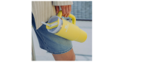 Persona en shorts vaqueros sostiene un vaso grande amarillo con asa y pajita y lleva puesta una chaqueta clara.