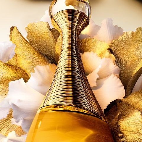 Un primer plano de un frasco de perfume dorado con un diseño texturizado en espiral, sobre un fondo de delicados pétalos blancos y dorados. La imagen irradia lujo y elegancia.