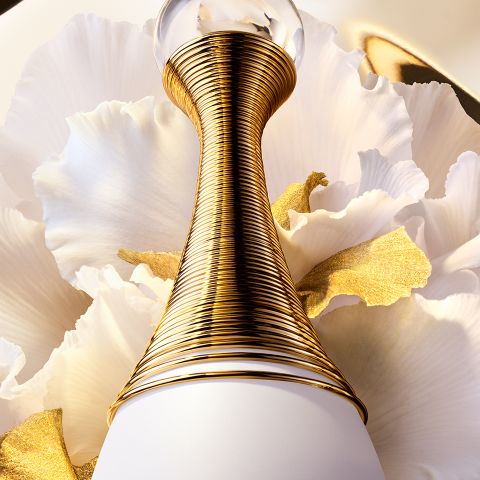 Un primer plano de un lujoso frasco de perfume con un cuello dorado en espiral sobre un fondo de suaves pétalos blancos, acentuado con toques de oro.