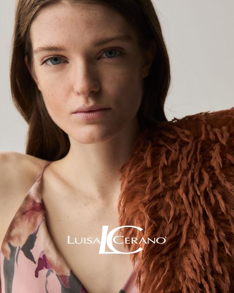 Una mujer con cabello castaño largo lleva un vestido floreado y una prenda de piel texturizada color óxido sobre el hombro. Mira directamente a la cámara. Abajo en el centro se ve el texto "Luisa Cerano".