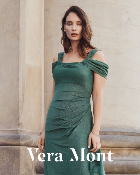 Una mujer con un vestido verde brillante sin hombros está de pie frente a una pared de piedra. El texto "Vera Mont" aparece en la parte inferior de la imagen.