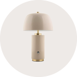 Eine moderne beigefarbene Tischleuchte mit zylindrischem Sockel, goldenen Akzenten und einem kuppelförmigen Schirm vor einem hellen, runden Hintergrund.