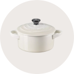 Ein Le Creuset Dutch Oven aus weißer Keramik mit Deckel und schwarzem Knauf, mit zwei seitlichen Griffen, dargestellt auf einem hellgrauen, runden Hintergrund.