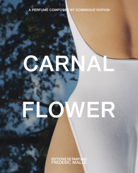 Primer plano de una persona en traje de baño blanco, con árboles borrosos al fondo. Un texto grande sobre la imagen dice "CARNAL FLOWER". En el texto adicional se menciona a Dominique Ropion y Editions de Parfums Frederic Malle.