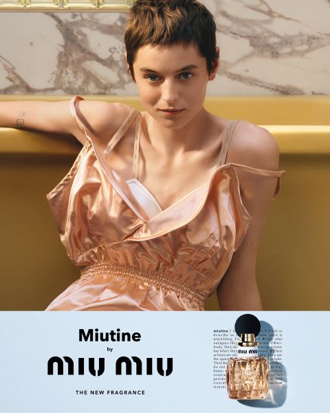 Una persona con pelo corto y un vestido rosa sedoso sin mangas sentada en un sofá amarillo. Debajo se ven un frasco de perfume Miu Miu y el texto "Miutine de MIU MIU LA NUEVA FRAGANCIA".