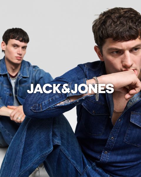 Dos hombres con atuendos de mezclilla están sentados frente a un fondo simple. El hombre de adelante se tapa la boca con la mano, mientras que el otro está sentado detrás de él. En el centro está el texto "JACK & JONES".