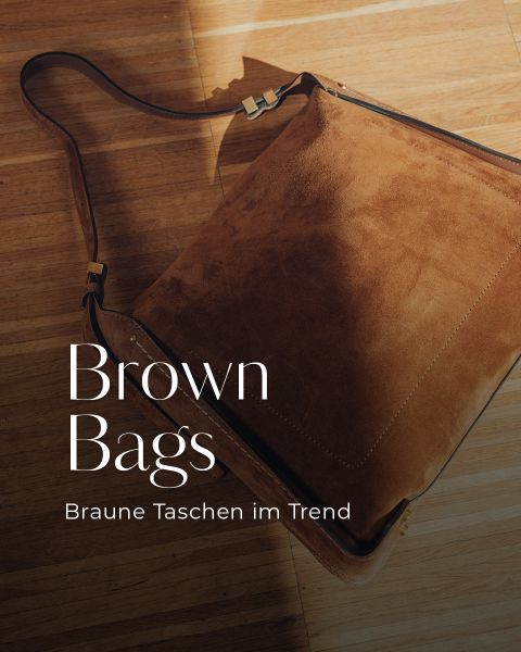Un bolso bandolera grande de gamuza marrón con herrajes dorados sobre un suelo de madera. El texto dice "Brown Bags" y "Bolsos marrones en tendencia".