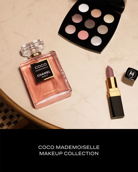Un frasco de perfume Coco Mademoiselle, un lápiz labial Chanel y una paleta de sombras de ojos sobre una superficie de mármol.